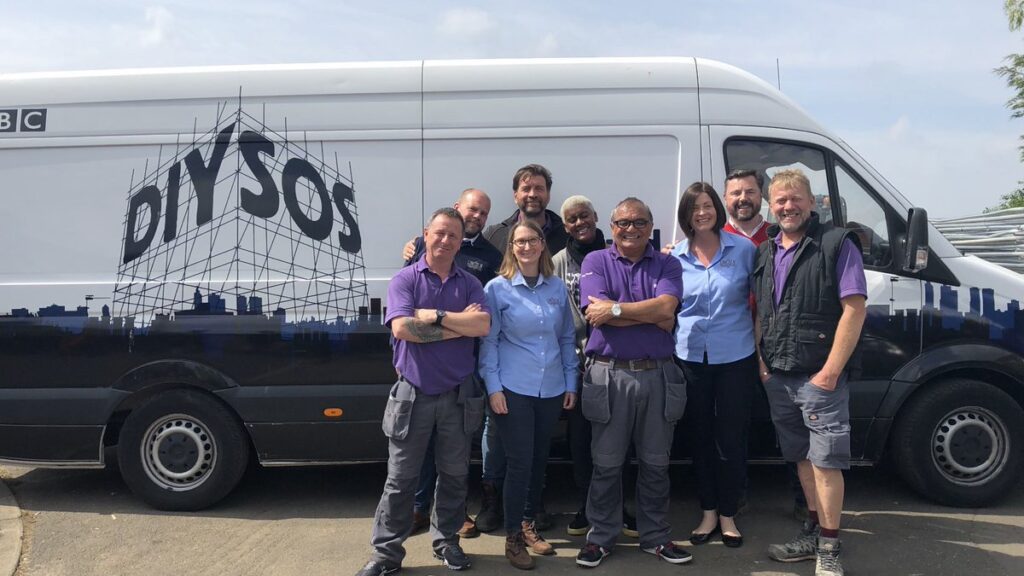 A group of men and woman in purple standing in front of a DIY SOS van